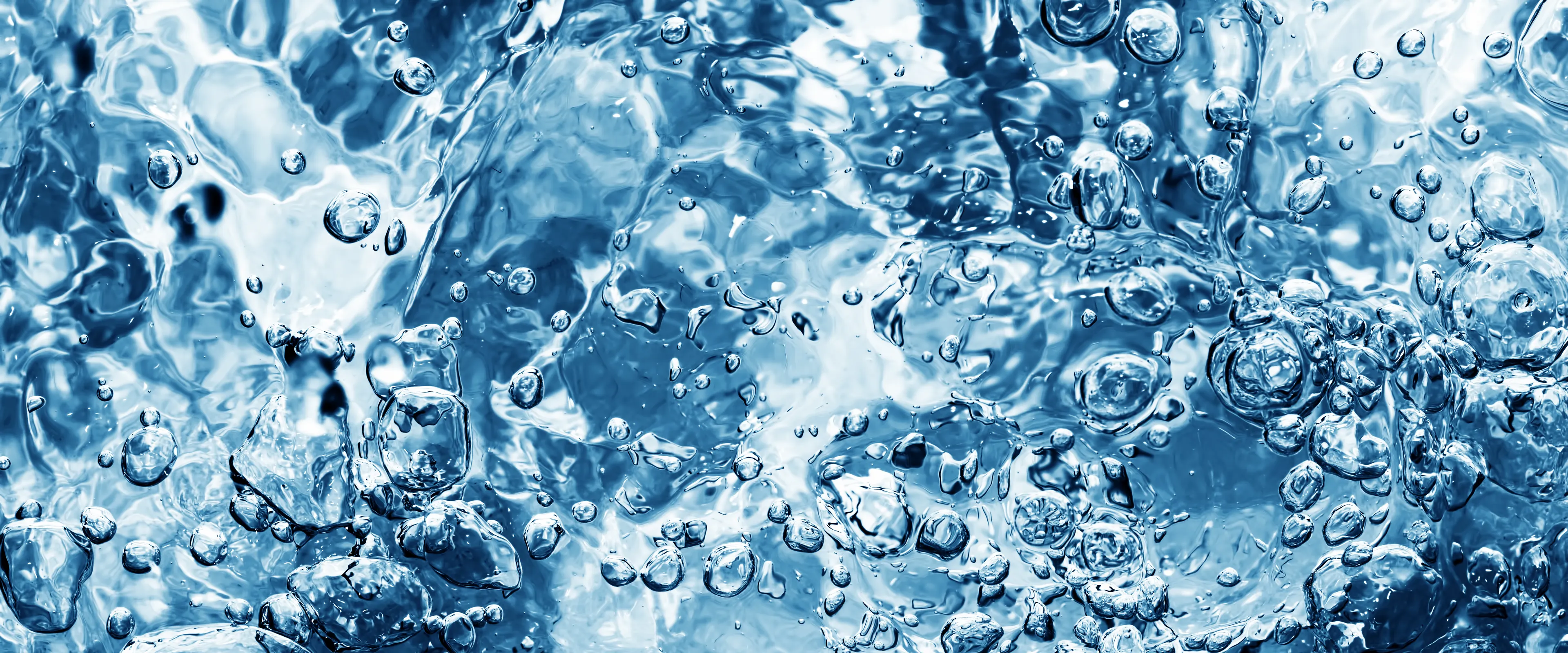 Close-up view of bubbling, clear blue water, showcasing swirling patterns and reflections. The image highlights the dynamic motion of the water and bubbles.