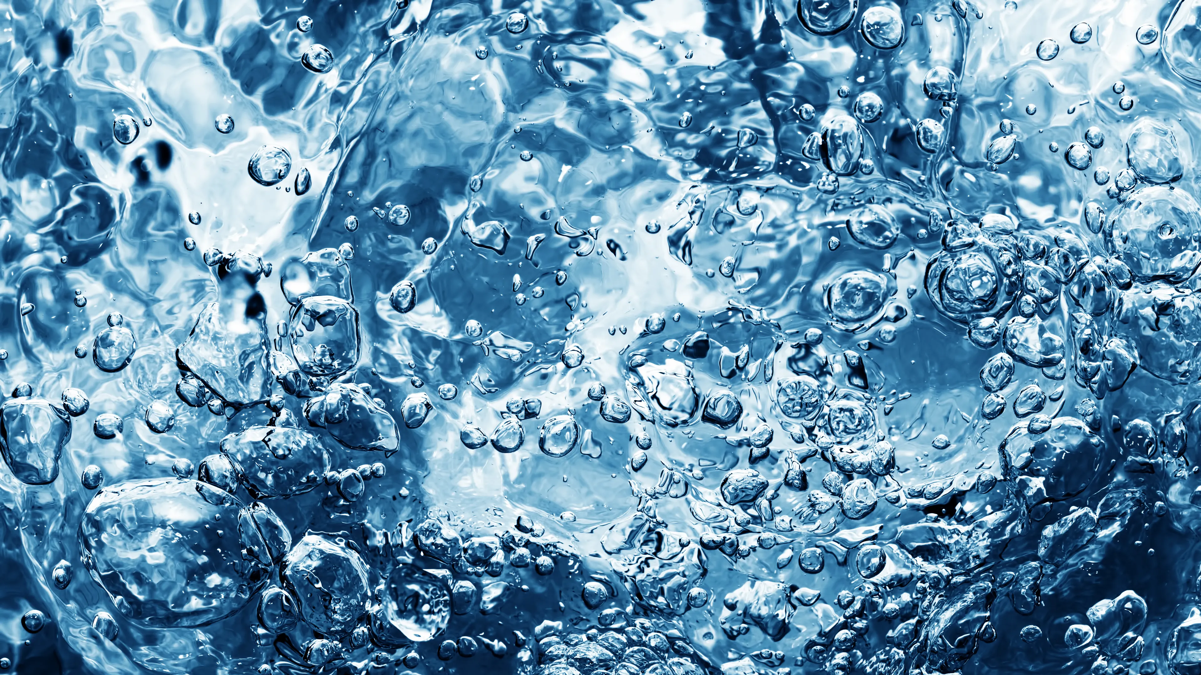Close-up view of bubbling, clear blue water, showcasing swirling patterns and reflections. The image highlights the dynamic motion of the water and bubbles.