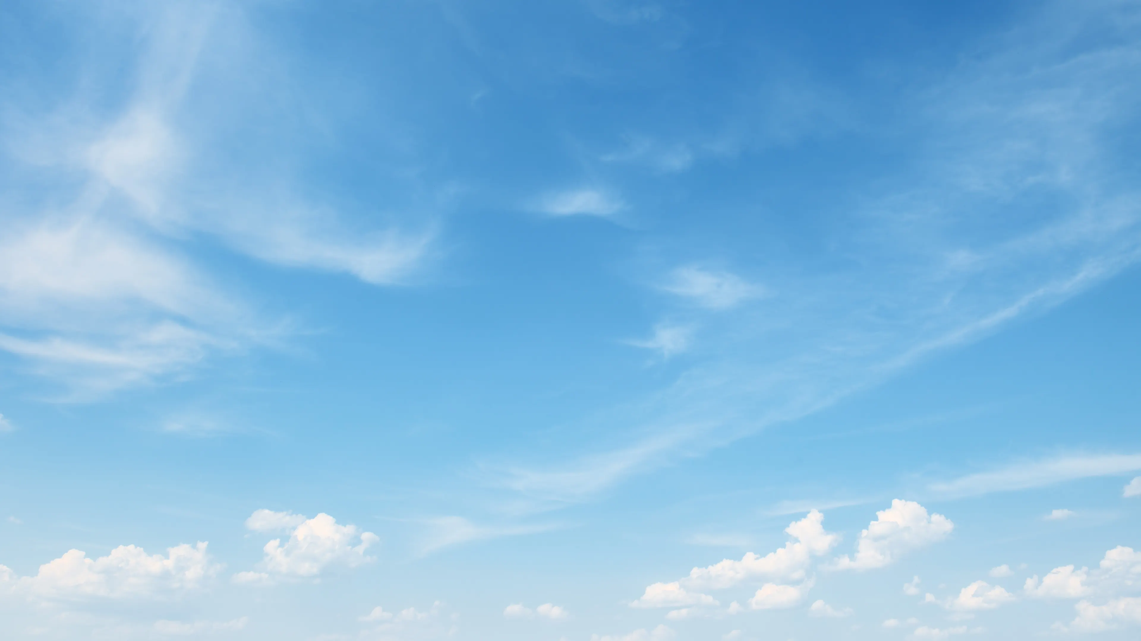 A clear blue sky with wispy white clouds scattered across. The clouds are thin and feathery, contrasting gently with the vibrant blue. The scene evokes a serene and peaceful atmosphere.