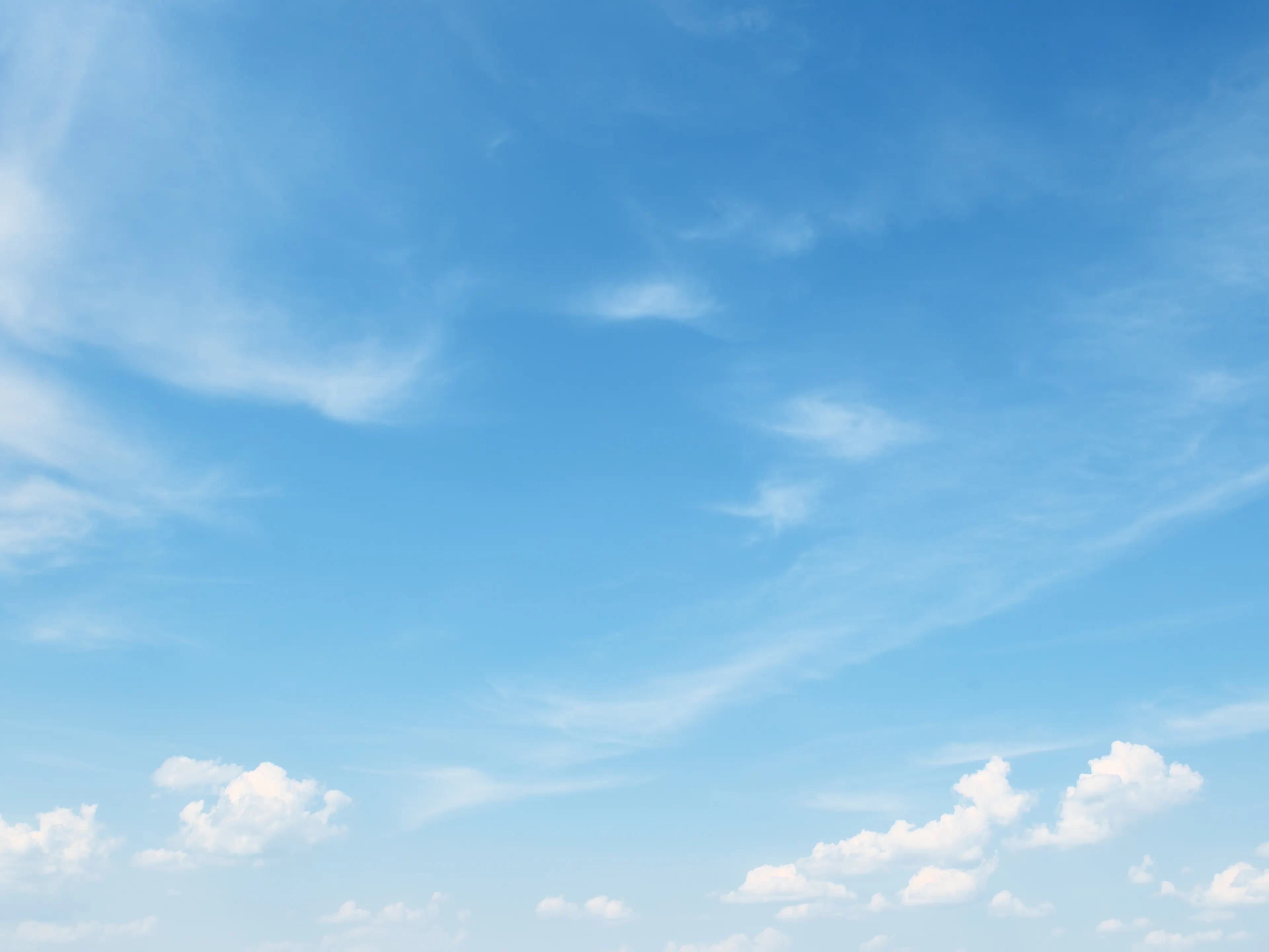 A clear blue sky with wispy white clouds scattered across. The clouds are thin and feathery, contrasting gently with the vibrant blue. The scene evokes a serene and peaceful atmosphere.