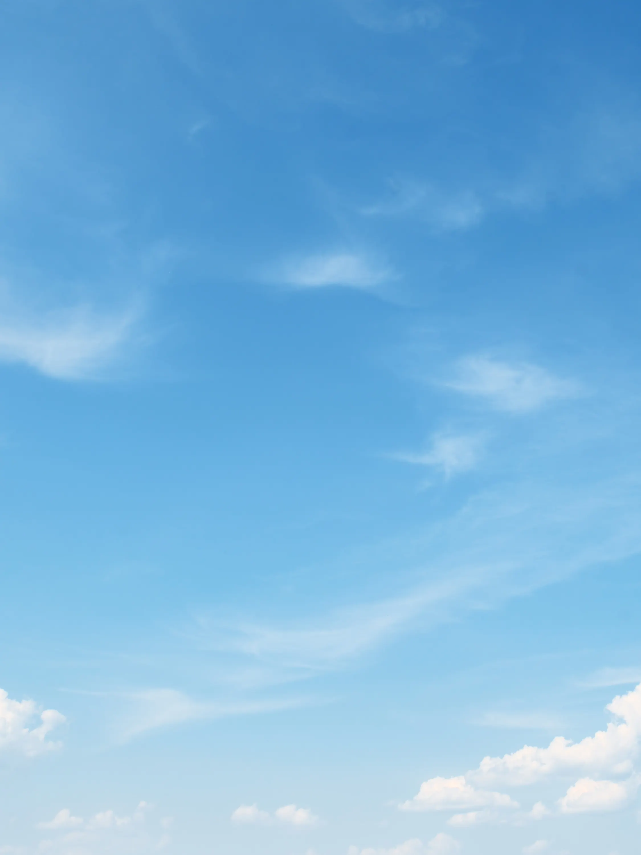 A clear blue sky with wispy white clouds scattered across. The clouds are thin and feathery, contrasting gently with the vibrant blue. The scene evokes a serene and peaceful atmosphere.