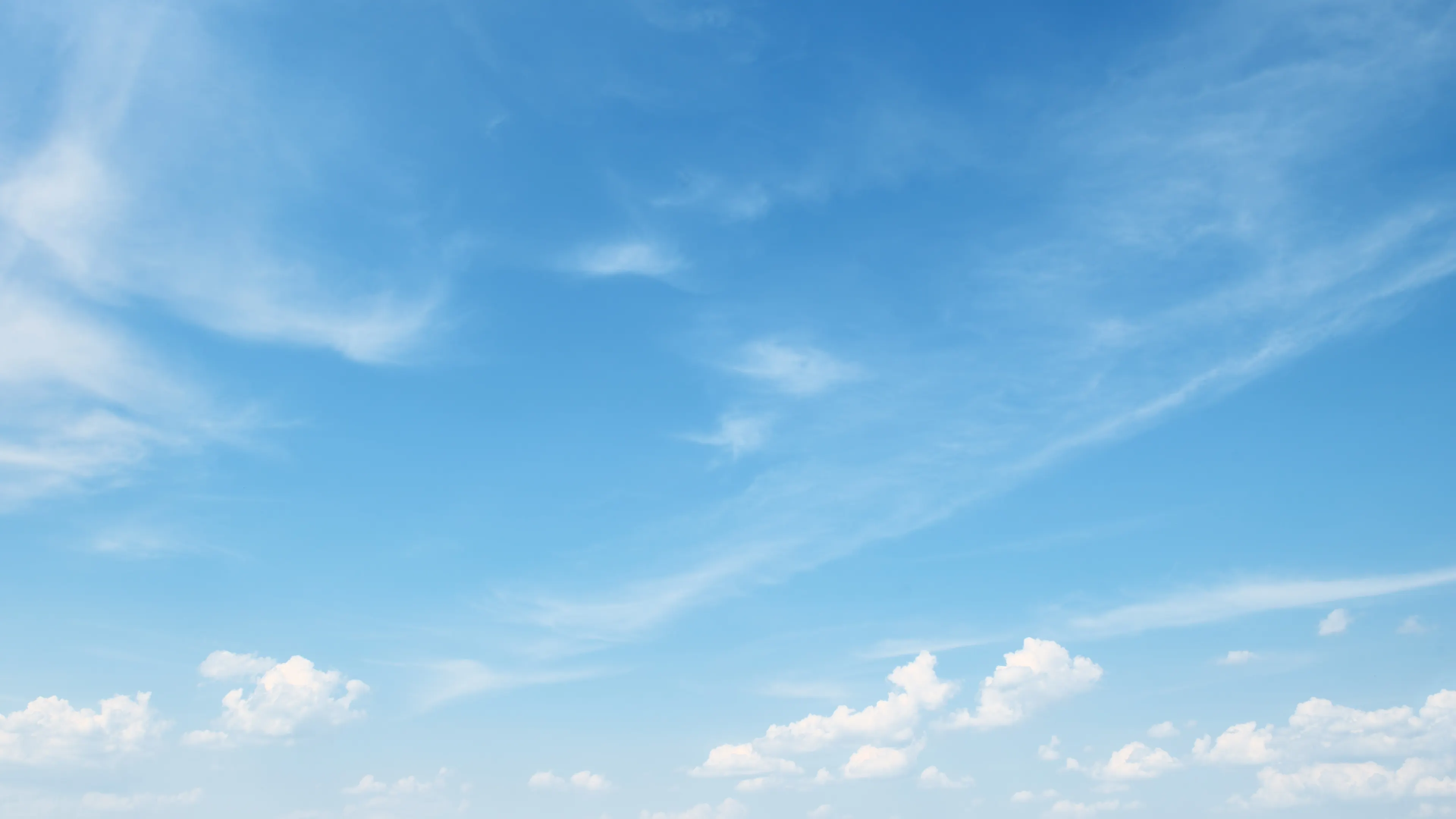 A clear blue sky with wispy white clouds scattered across. The clouds are thin and feathery, contrasting gently with the vibrant blue. The scene evokes a serene and peaceful atmosphere.